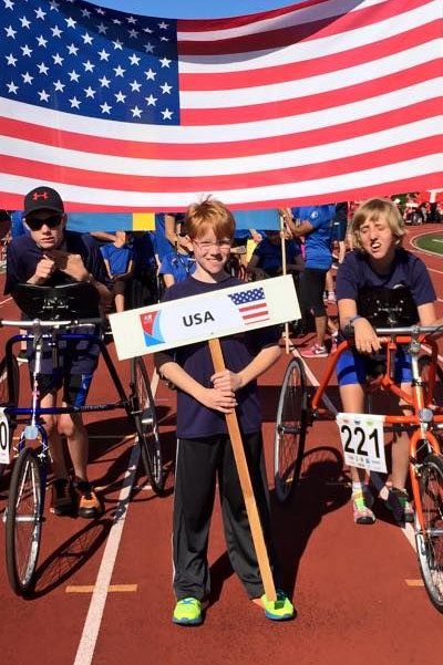 young boy holding USA sign with kids in the background and american flag